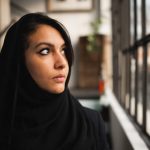 Close-up of young attractive arab woman wearing a black veil. Female profile looking out the window with serious face.